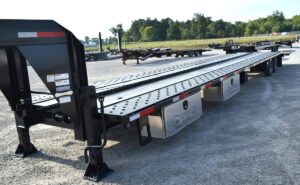A long, gray 53-foot gooseneck trailer, a flatbed style trailer designed for heavy hauling. The trailer has tandem axles and a low-profile deck, and is shown in a clean, industrial setting, highlighting its immense length.